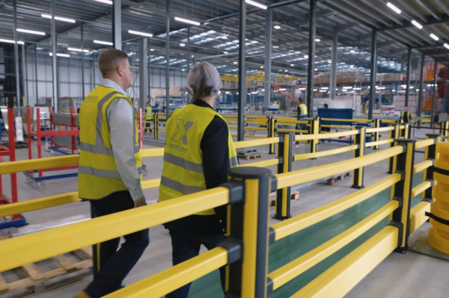 Safety barriers protecting pedestrian walkways in a modern warehouse, with workers in yellow safety vests.