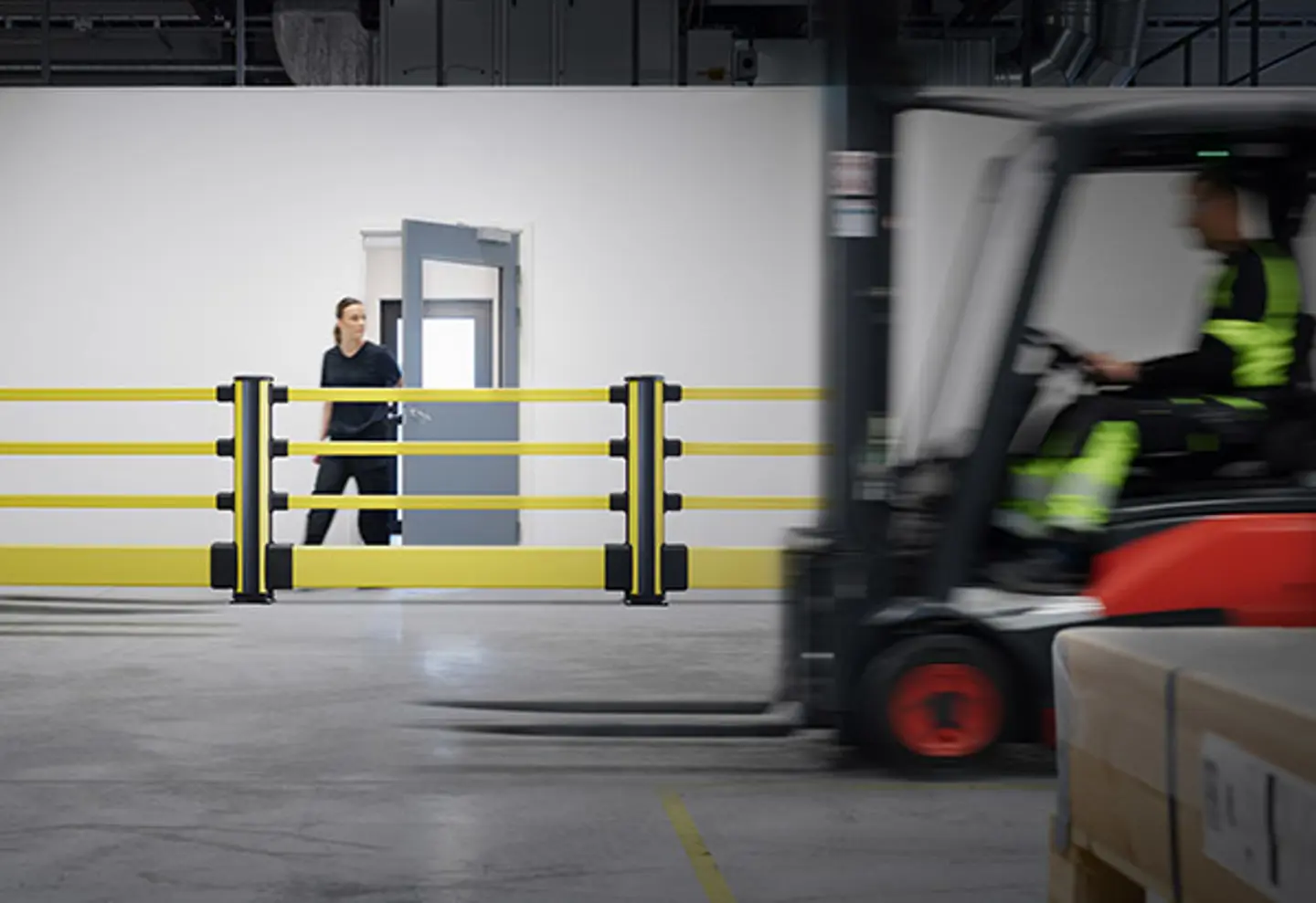 A forklift is shown moving past a pedestrian protected by yellow Axelent barriers 