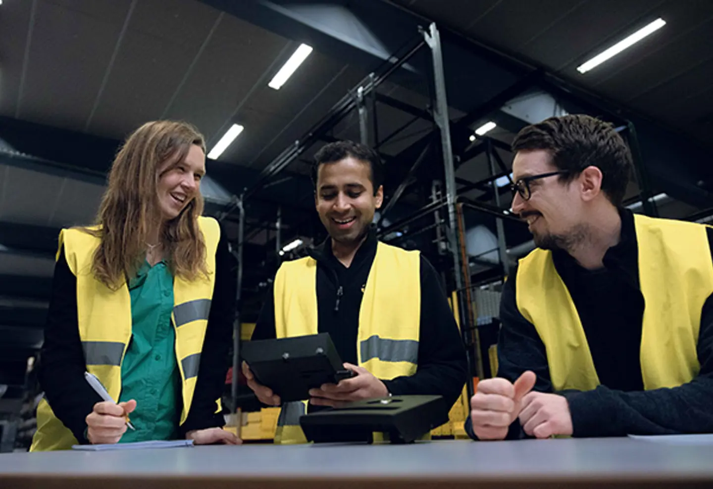 Three people are shown in a warehouse environment chatting and smiling.